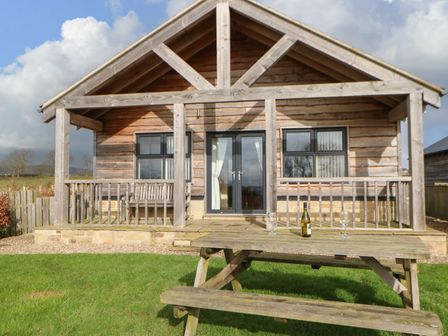 A wooden cabin with a porch and a picnic table on a lawn at Coquet in Longframlington near Alnwick