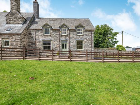 Stone house with green door and windows behind wooden fence and grass at Waedog Bach in Rhos-y-Gwaliau near Bala