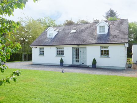 A white detached house with a gray roof and a grassy front yard at Woodbine Cottage in Old Leighlin near Kilkenny County Kilkenny
