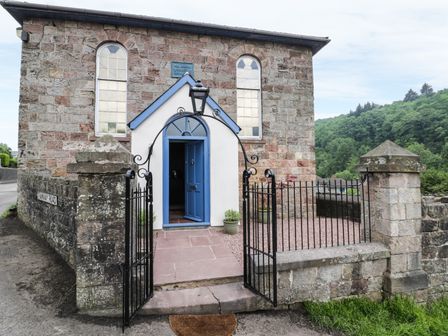 Stone building with blue door and wrought iron gate on pathway at Rainforest Chapel in Ruspidge