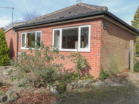 A brick house with multiple windows and plants in front at The Lodge in Coltishall