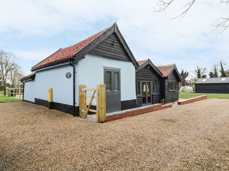 The exterior of a house with blue and black walls a red tiled roof a wooden gate and gravel driveway at Whitehands Farm Barn in Old Buckenham