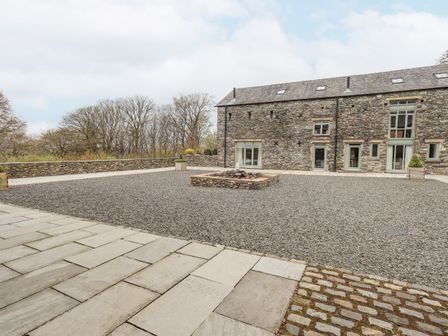 An outdoor courtyard with a stone building and gravel area with fire pit at Oak Cottage in Backbarrow