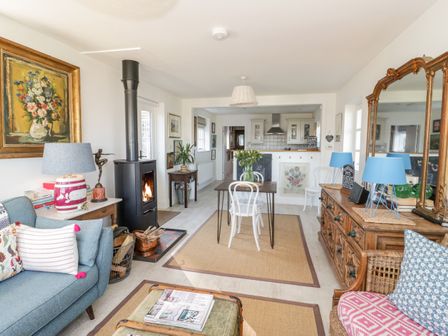 A living and dining area with a blue sofa a wood burning stove a dining table with white chairs and a large mirror above a wooden dresser at Bronwen Lodge in Conwy