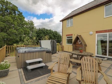 A patio with a hot tub wooden chairs a wooden picnic table and a wooden shelter at Foxes Meadow in Howey near Llandrindod Wells