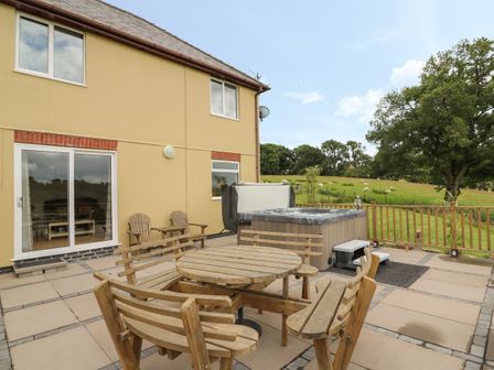 An outdoor patio with wooden seating, a hot tub, and a view of a grassy field with trees at Pheasant Wood in Howey near Llandrindod Wells