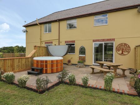 A backyard patio with a wooden hot tub wooden picnic table and bench and a decorative wall hanging at Owl Cottage in Llandrindod Wells