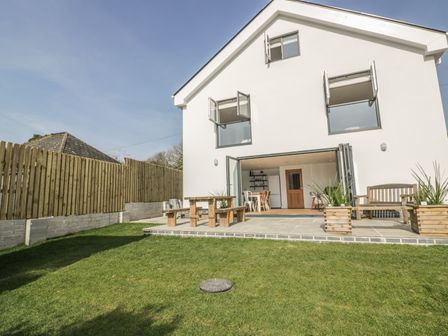 A backyard with a lawn wooden picnic table outdoor bench and an open patio door leading to a dining area at The Beach Halt in Perranporth