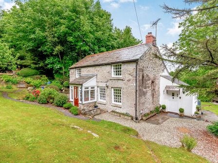 A stone cottage with a lawn and garden surrounded by trees at Westside Cottage in Cardinham near Bodmin