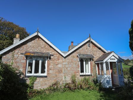 A stone cottage with two windows and a porch entrance with glass panels at Pabo Lodge in Llandudno Junction near Llandudno