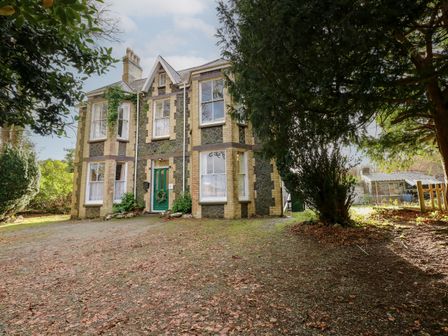 A stone and brick house with a green door surrounded by trees and a gravel driveway at Plas Dorothea in Talysarn near Penygroes