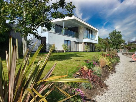 A modern two-story house with glass balconies and a garden with plants and a gravel path at Ancarva Near Kingsands