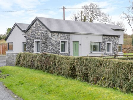 A single story house with stone and white exterior walls and green door behind a trimmed hedge at River Dale in Sligo Town