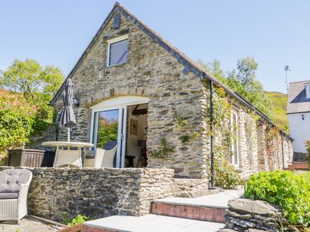 A stone cottage with outdoor seating and greenery at The Barn at Waen y Ffynnon in Ruthin