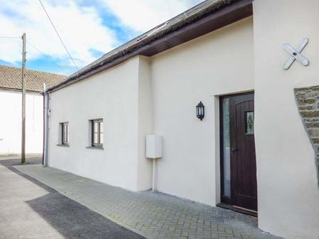 Exterior view of a building with two small windows and a dark brown door on a paved walkway at Honeysuckle Cottage Ashwater near Holsworthy