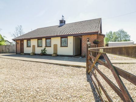 A single-story house with multiple windows and a tiled roof behind a wooden gate with gravel driveway at Kingfisher Wattisfield near Rickinghall and Diss
