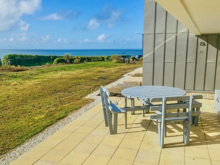 An outdoor patio with a round table and chairs overlooking a grassy area and the sea at Saltwater One Lusty Glaze in Newquay