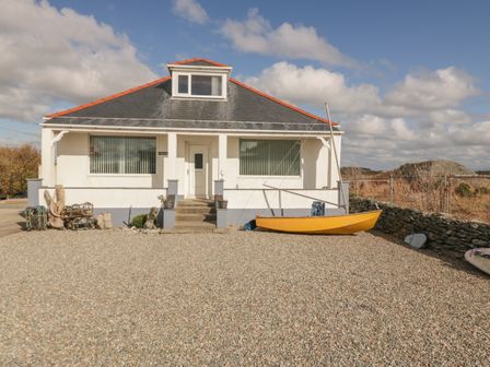 A white house with a small set of stairs and a yellow sailboat in front at Coed Llai in Trearddur Bay