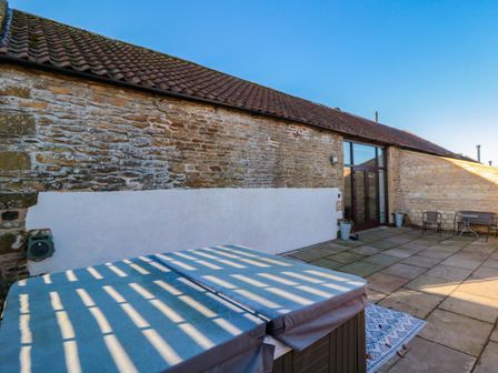 A stone courtyard with a covered hot tub table and chairs at The Old Workshop in Suffield near Scarborough