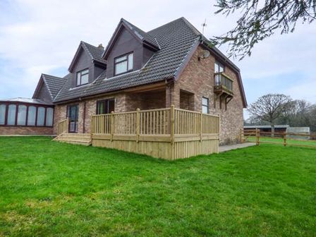 A brick house with a tiled roof wooden deck and green lawn at Cwm Gran Meadows in Llanharry