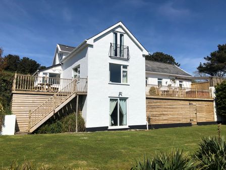 A white house with wooden decks and balconies surrounded by grass and trees at Valley View in Ilfracombe