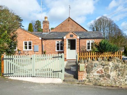 A brick house with a white wooden gate and a stone wall at Kitts Cottage in Little Malvern near Malvern