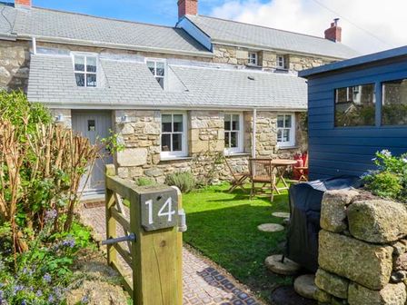 A stone cottage with a gray door and windows a garden with a table and chairs and a blue shed at 14 Boscaswell Downs in Pendeen near St Just