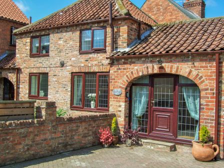 A brick exterior of a house with tiled roof wooden framed windows and a wooden door with potted plants at The Old Dairy in Beverley