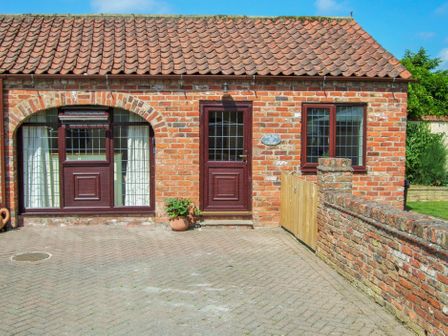A brick cottage with a tiled roof wooden doors and windows and a small potted plant at Oak Tree Cottage in Beverley