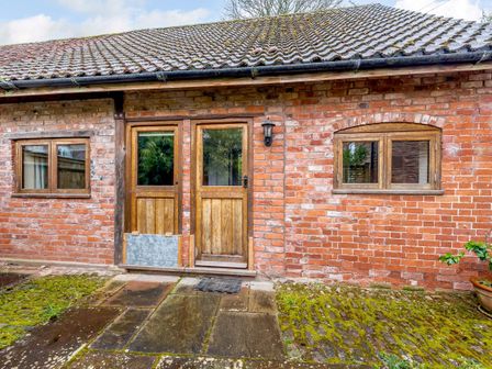 A brick building exterior with two wooden doors and two wooden windows at The Bothy in Phocle Green near Ross-on-Wye