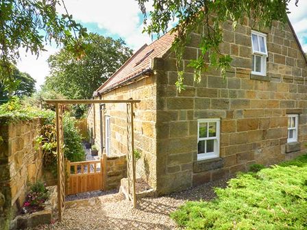 A stone cottage with a wooden gate and garden area at Quakers Cottage in Hinderwell near Runswick Bay