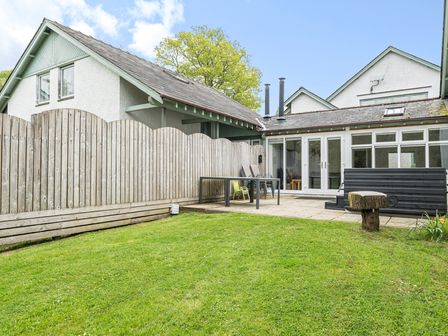 A fenced backyard with a lawn table and stacked chairs patio doors on a house at Hazel - Woodland Cottages in Windermere
