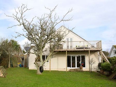 A backyard with a tree and tire swing and a two story house with balcony and sliding doors at Summerfield House with Hot Tub in Gorran Haven