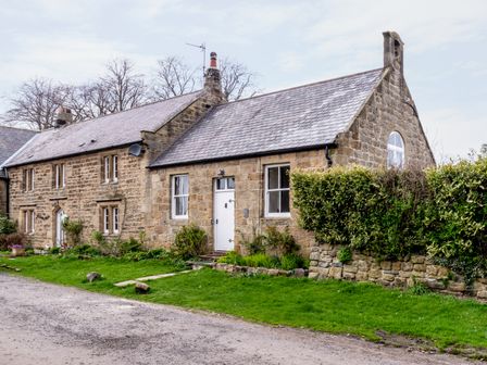 A stone cottage with white doors and windows and a hedge along the side at The Old School Room in Longhorsley near Morpeth and Alnwick