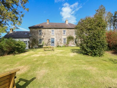 A stone house with multiple windows and a blue door with a grassy lawn and trees at Ballintlea near Dungarvan County Waterford