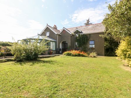 A house with a glass conservatory and garden with plants and grass at Rhianfa in Aberdaron