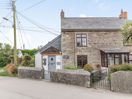 A stone cottage with a grey door and windows with a garden behind a low stone wall at Victoria Cottage in St Newlyn East near Newquay