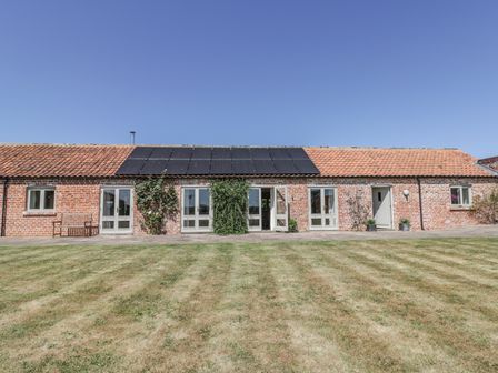 A brick building with multiple doors and windows a tiled roof with solar panels and a lawn in front at Cow Byre in Malton