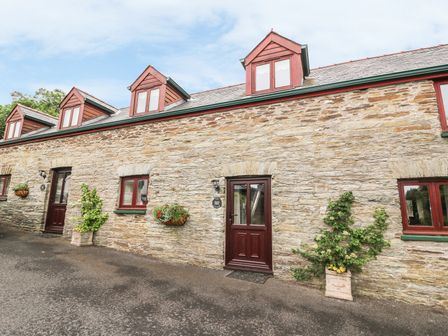 Stone cottage exterior with red framed windows and doors and potted plants outside Ash Cottage in Newcastle Emlyn