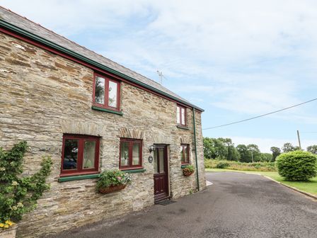 A stone cottage with red framed windows and flower boxes on a paved driveway near greenery at Oak Cottage Bryngwenith near Newcastle Emlyn