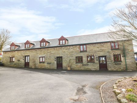 A row of stone houses with multiple windows and doors surrounded by trees at Cherry Cottage in Bryngwenith near Newcastle Emlyn