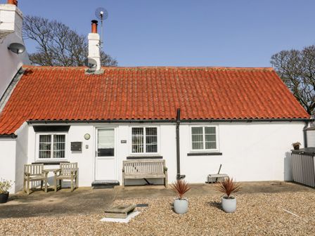 A single story white house with red tiled roof windows a door outdoor wooden chairs and potted plants at The Old Joiners Shop in Barmston near Bridlington