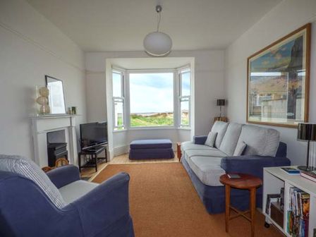 A living room with sofas a television a fireplace and a large window showing greenery at Sandy Bank in Rhosneigr
