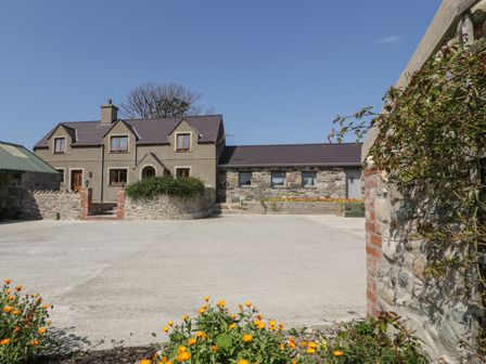 An exterior view of a two-story house with stone and plaster walls and a driveway with flowers in the foreground at Caer Moel in Caernarfon