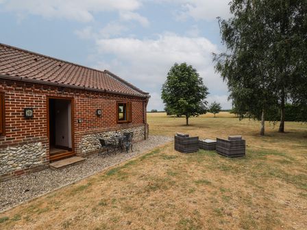 A patio area with chairs and a table beside a brick house at The Annexe in Litcham