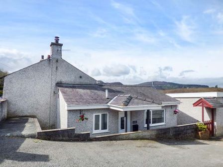 A single story house with two windows and a chimney with hills in the background at Arfryn in Bethesda