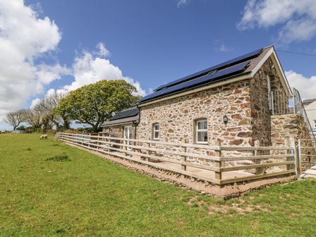 Stone house with wooden fence and green lawn under blue sky at Beudy Tyddyn in Llanerchymedd