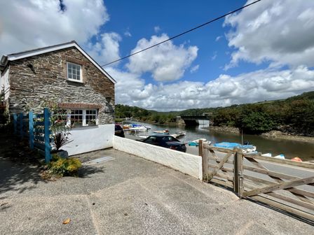 A stone house next to a river with boats and a wooden gate at The Boat House in Golant near Tywardreath