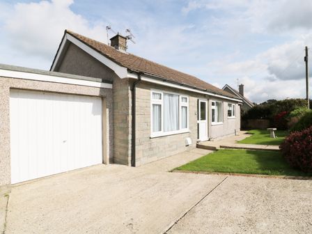 A bungalow with attached garage and front lawn with bushes at Bungalow in Fishguard