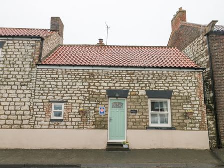 A stone cottage with a green front door and two windows at Amari in Staxton